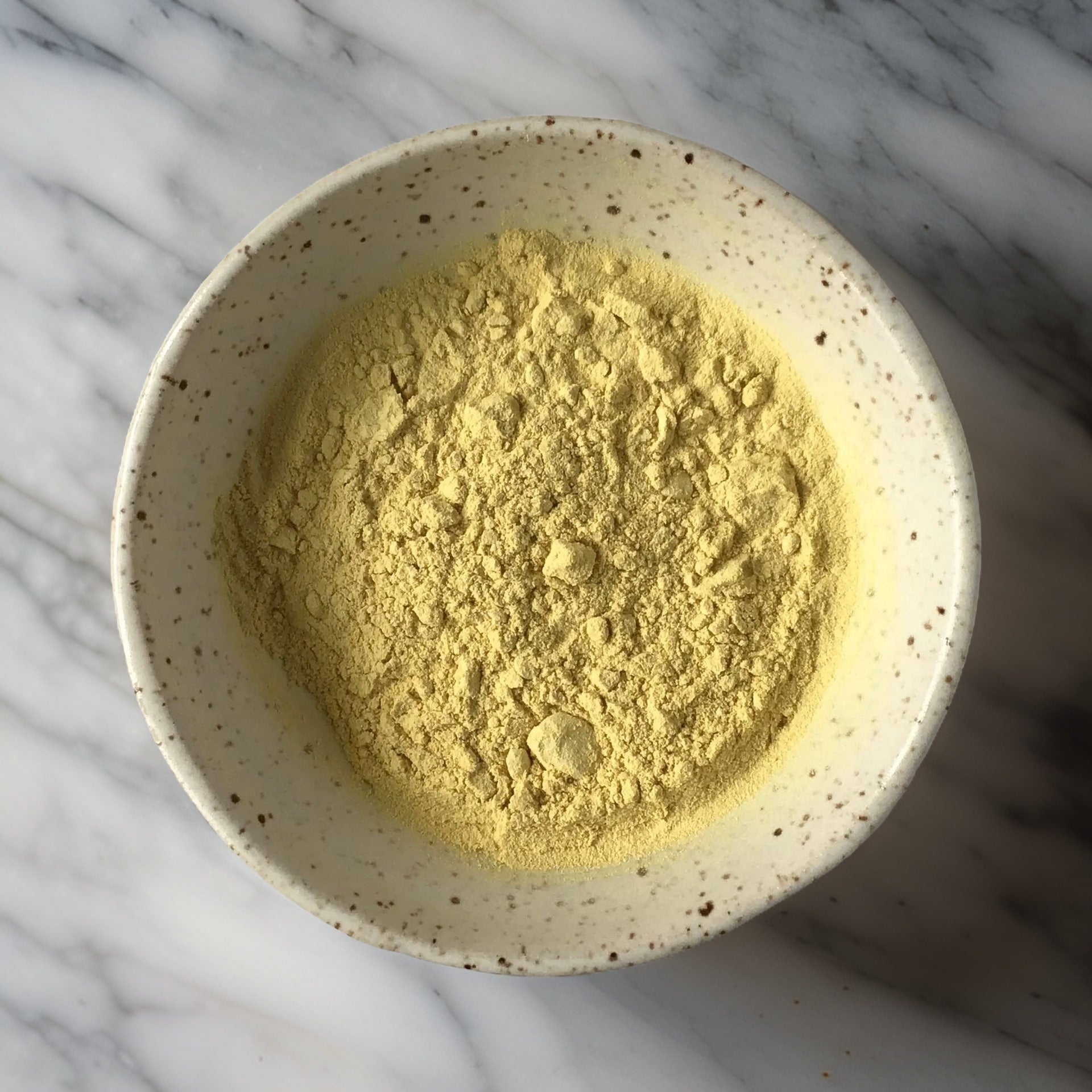 A rustic white speckled bowl showcasing Pine Pollen powder. The light-yellow powder has a fine, airy texture, making it easy to mix into liquids for consumption.